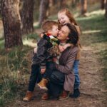 Une mère avec ses enfants en forêt qui font un câlin et des bisous.