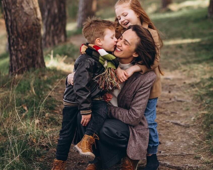 Une mère avec ses enfants en forêt qui font un câlin et des bisous.
