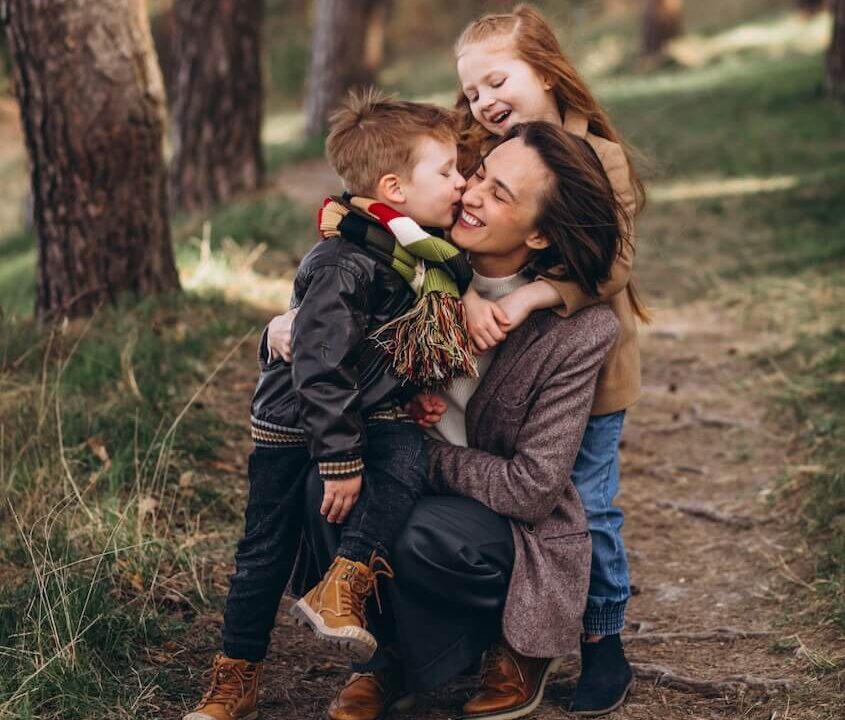 Une mère avec ses enfants en forêt qui font un câlin et des bisous.