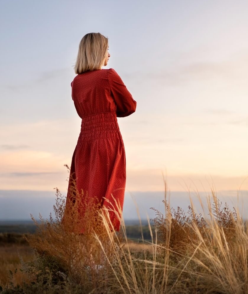 Femme en robe rouge sur une dune qui regarde au loin.
