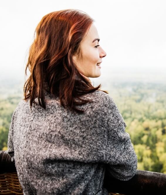 Femme qui a recours à la naturopathie et regarde au loin la nature et les arbres et sourit.
