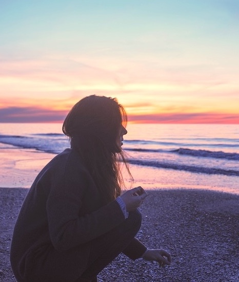 Jeune femme regardant un coucher de soleil sur la mer et qui regarde à l'horizon en réfléchissant à ce qu'elle veut faire de sa vie, quelle décision ou choix elle doit faire pour être heureuse.