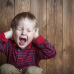 Enfant accroupi en train de crier fort et de se boucher les oreilles