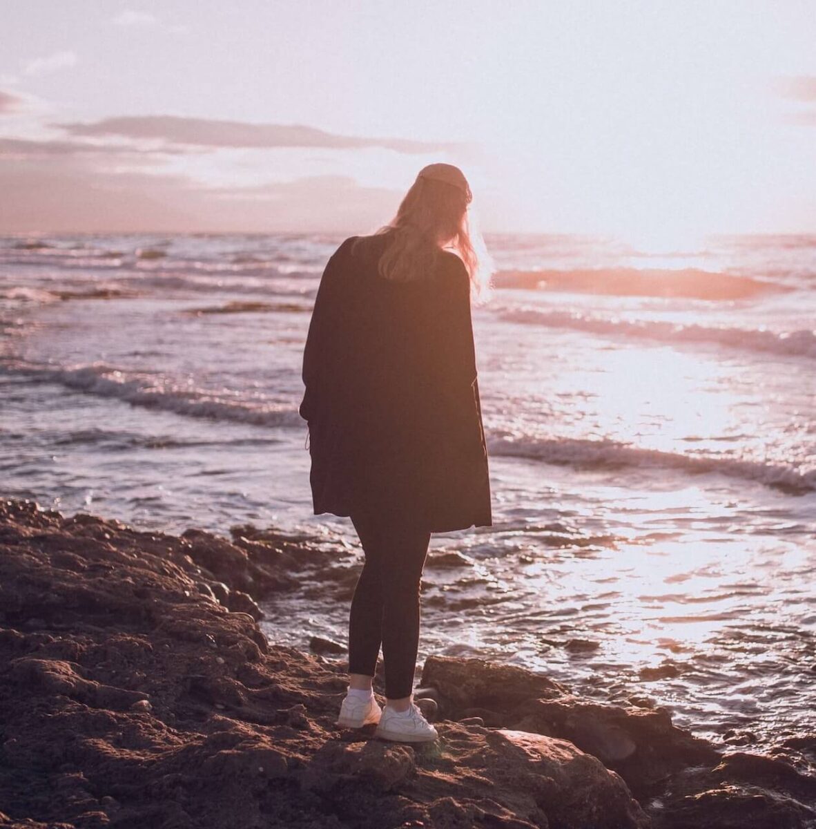 Femme face à la mer au coucher du soleil et qui réfléchit.