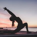 Femme au lever du soleil sur la plage qui fait des étirements le matin avant sa journée de travail, avec une posture de yoga