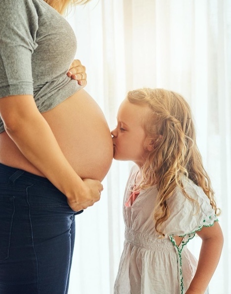 Petite fille qui fait un bisous sur le ventre de sa maman enceinte.