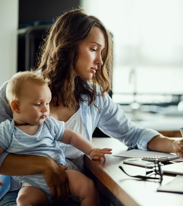 Femme qui travaille sur son bureau avec son ordinateur tout en s'occupant de son bébé.