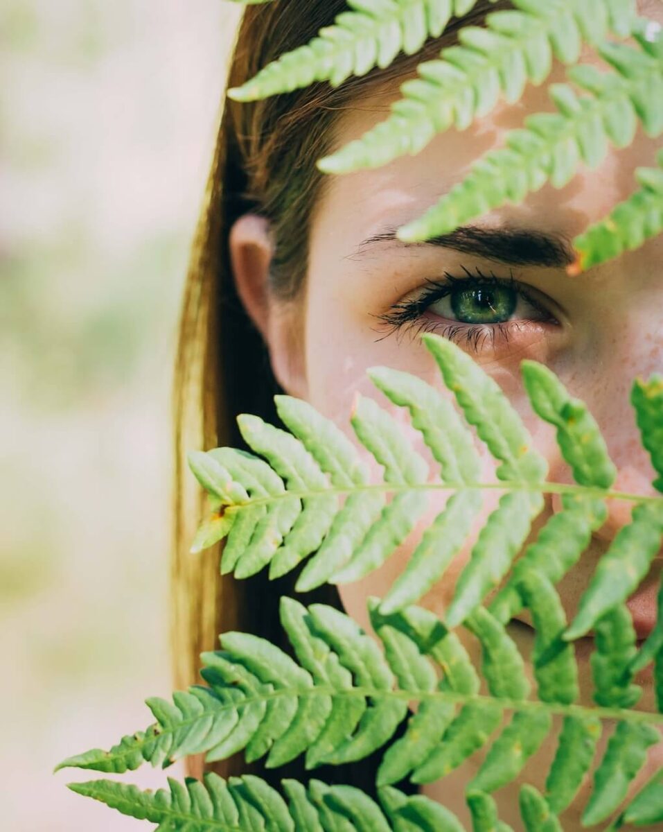 Portrait de femme qui regarde à travers les feuilles d'une plante, symbolisant la naturopathie