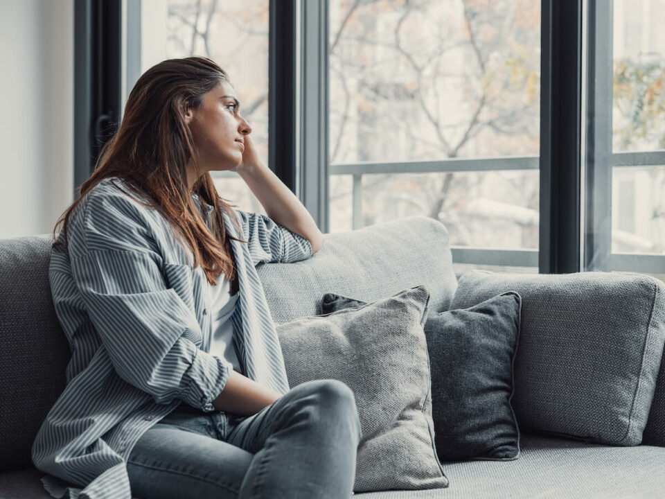 Femme qui a des pensées négatives, assise sur son canapé en regardant par la fenêtre